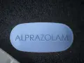 Niebieska tabletka z napisem ALPRAZOLAM na ciemnym tle.
