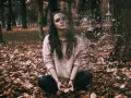 Kobieta w swetrze siedzi na jesiennych liściach, jej ciało rozpada się na fragmenty.