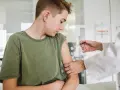Chłopiec w zielonej koszulce otrzymuje szczepienie od lekarza w białym fartuchu.