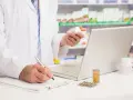 Farmaceuta sprawdza w komputerze pradaxa zamiennik, trzymając w dłoni buteleczkę leku.