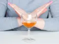 Ręce w geście "stop" nad kieliszkiem z bursztynowym płynem. Pytanie: czy po szczepieniu można pić alkohol? Odpowiedź brzmi: nie.