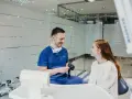 Dentysta w niebieskim uniformie rozmawia z pacjentką, sugerując nowy lek na ból zęba.