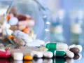 Kapsułki i tabletki rozsypane z naczynia laboratoryjnego. Wśród nich zielono-biała kapsułka, która może być antybiotykiem na grypę.