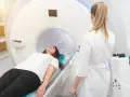 Pacjentka leży na stole do rezonansu magnetycznego, przygotowując się do badania. Lekarka czuwa obok.