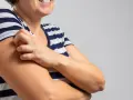 Kobieta w pasiastym T-shircie drapie się po ramieniu, doświadczając bardzo nietypowe objawy menopauzy, takie jak swędzenie skóry.
