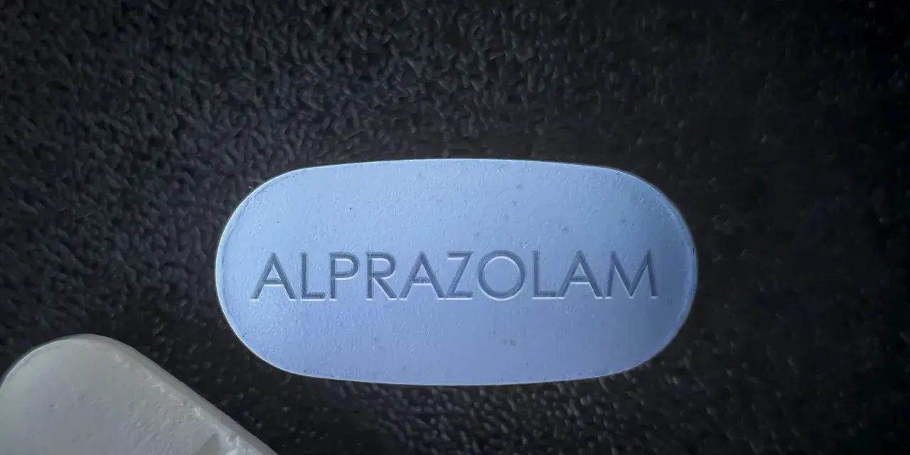 Niebieska tabletka z napisem ALPRAZOLAM na ciemnym tle.