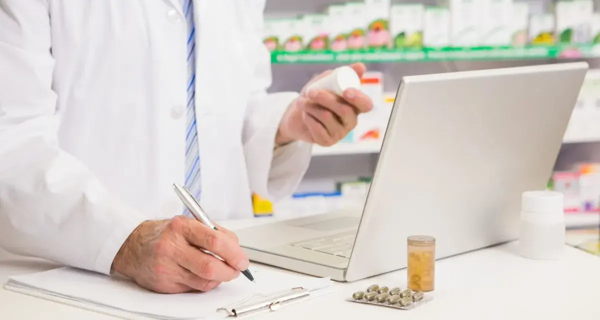 Farmaceuta sprawdza w komputerze pradaxa zamiennik, trzymając w dłoni buteleczkę leku.