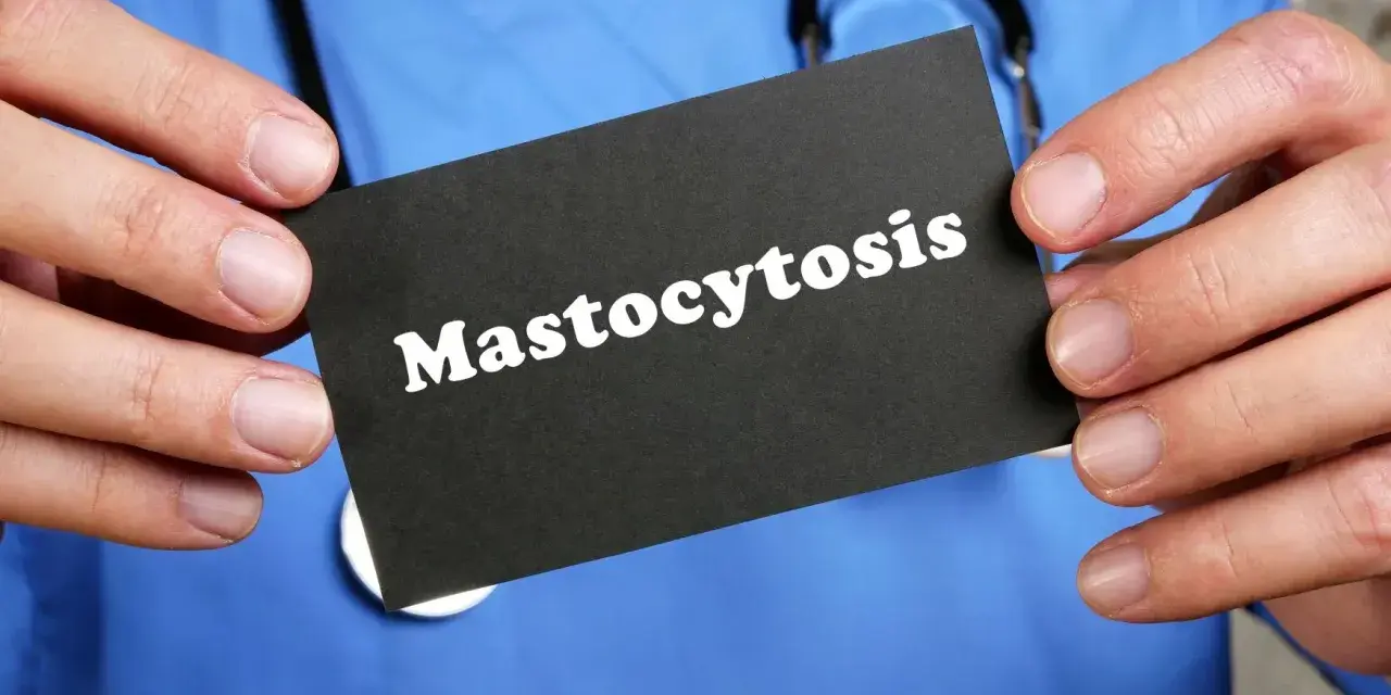 Lekarz w niebieskim kitlu trzyma kartę z napisem "Mastocytoza".