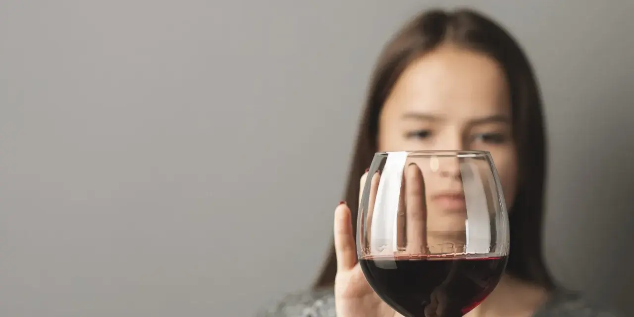 Kobieta odrzuca kieliszek z czerwonym winem, symbolizując walkę z pokusą, która może prowadzić do dawki śmiertelnej alkoholu.