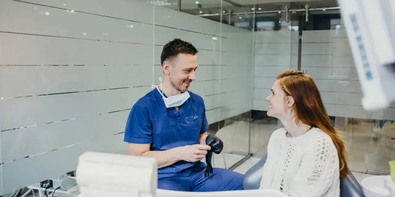 Dentysta w niebieskim uniformie rozmawia z pacjentką, sugerując nowy lek na ból zęba.
