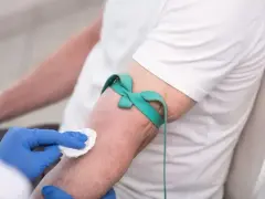 Ręka pacjenta z opaską uciskową i wacikiem, przygotowywana do pobrania krwi.