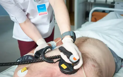 Ratownik medyczny wykonuje kardiowersję, przykłada elektrody defibrylatora do klatki piersiowej pacjenta, by przywrócić prawidłowy rytm serca.