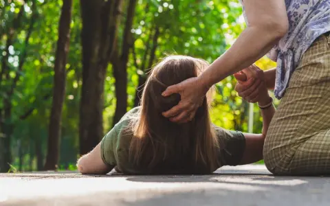 Osoba na ziemi, pomagająca jej druga osoba. Czy padaczka jest uleczalna? Ta scena budzi pytania o zdrowie i wsparcie.