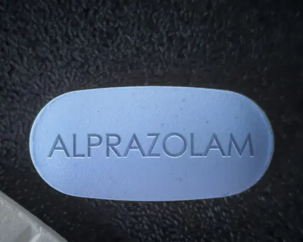 Niebieska tabletka z napisem ALPRAZOLAM na ciemnym tle.