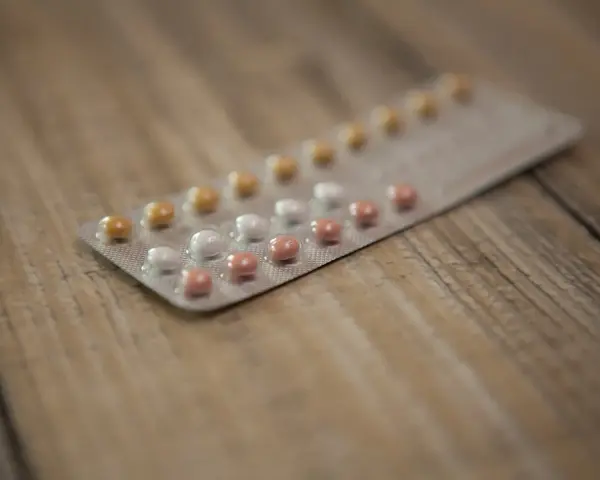 Opakowanie tabletek antykoncepcyjnych z białymi, różowymi i żółtymi pigułkami na drewnianym tle.