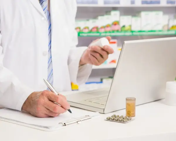 Farmaceuta sprawdza w komputerze pradaxa zamiennik, trzymając w dłoni buteleczkę leku.