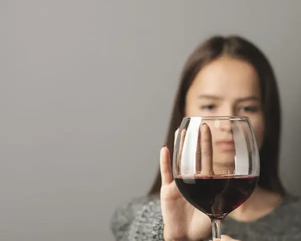 Kobieta odrzuca kieliszek z czerwonym winem, symbolizując walkę z pokusą, która może prowadzić do dawki śmiertelnej alkoholu.