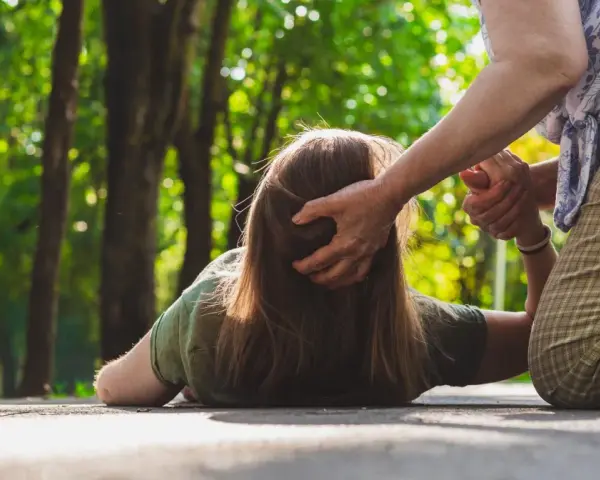 Osoba na ziemi, pomagająca jej druga osoba. Czy padaczka jest uleczalna? Ta scena budzi pytania o zdrowie i wsparcie.
