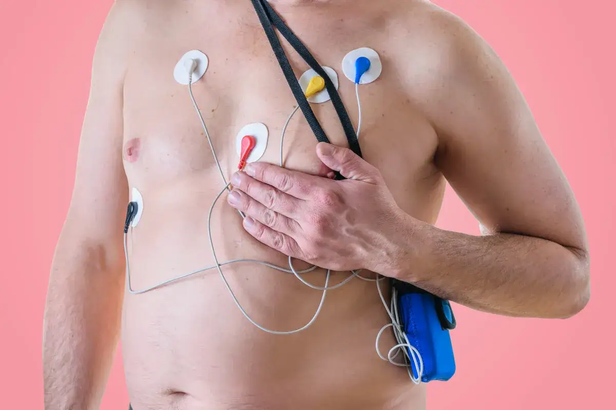 Mężczyzna z elektrodami na klatce piersiowej, podłączonymi do urządzenia. To badanie, co to ekg, monitoruje pracę serca.