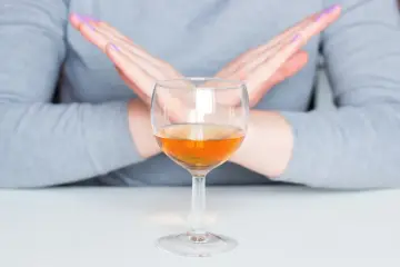Ręce w geście "stop" nad kieliszkiem z bursztynowym płynem. Pytanie: czy po szczepieniu można pić alkohol? Odpowiedź brzmi: nie.