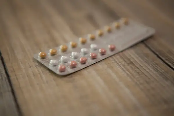 Opakowanie tabletek antykoncepcyjnych z białymi, różowymi i żółtymi pigułkami na drewnianym tle.
