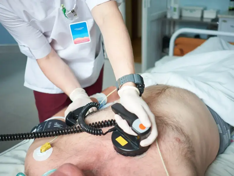 Ratownik medyczny wykonuje kardiowersję, przykłada elektrody defibrylatora do klatki piersiowej pacjenta, by przywrócić prawidłowy rytm serca.