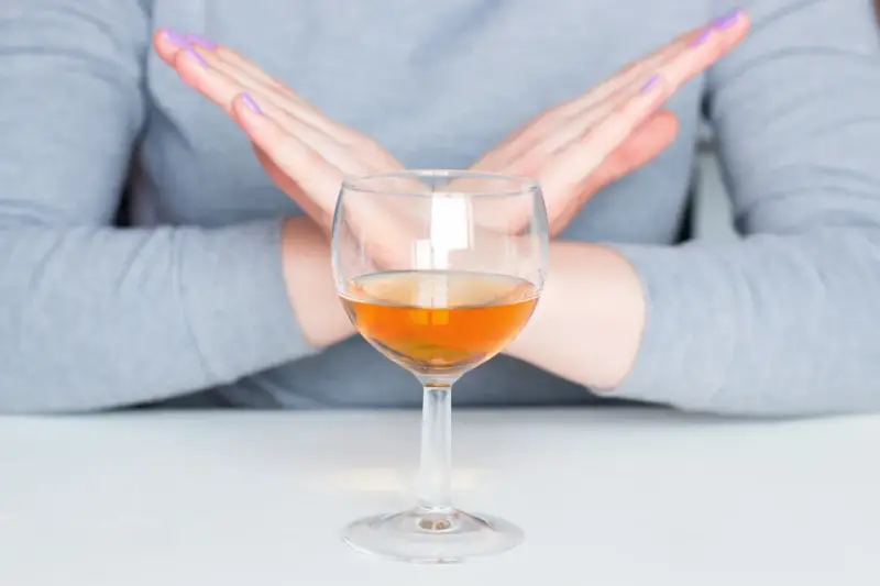 Ręce w geście "stop" nad kieliszkiem z bursztynowym płynem. Pytanie: czy po szczepieniu można pić alkohol? Odpowiedź brzmi: nie.
